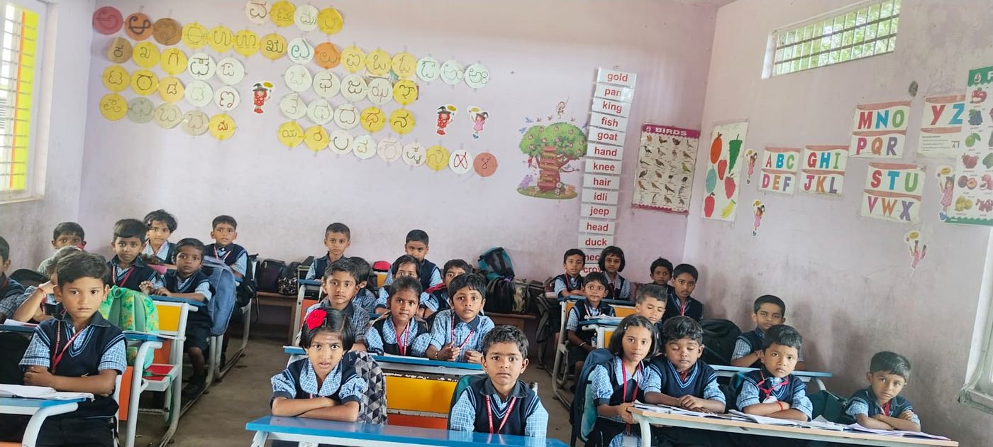 Primary students in a classroom with Kannada and English alphabet charts